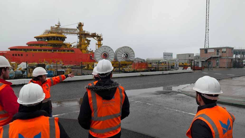 GREENOFFPORT project team touring Montrose Port in safety gear, with an offshore vessel and cable-handling equipment in the background