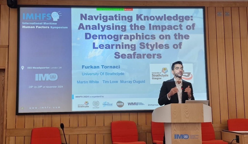 Furkan Tornaci presenting research on seafarer learning styles at IMHFS 2024 in the IMO Headquarters auditorium in London